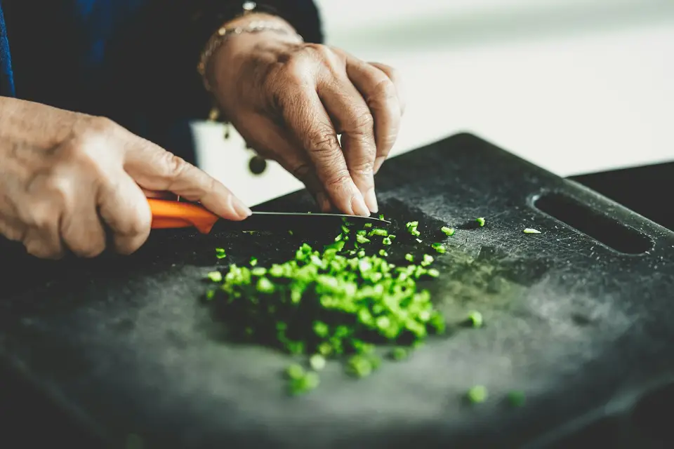 A pair of hands chopping spring onions on a dark cutting board.