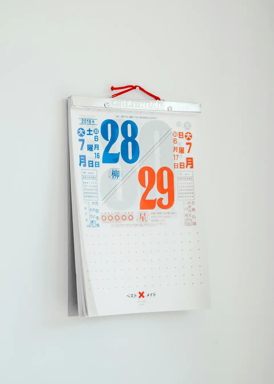 A tear-off wall calendar hanging by a red cord on a plain white wall, showing the 28th and 29th.