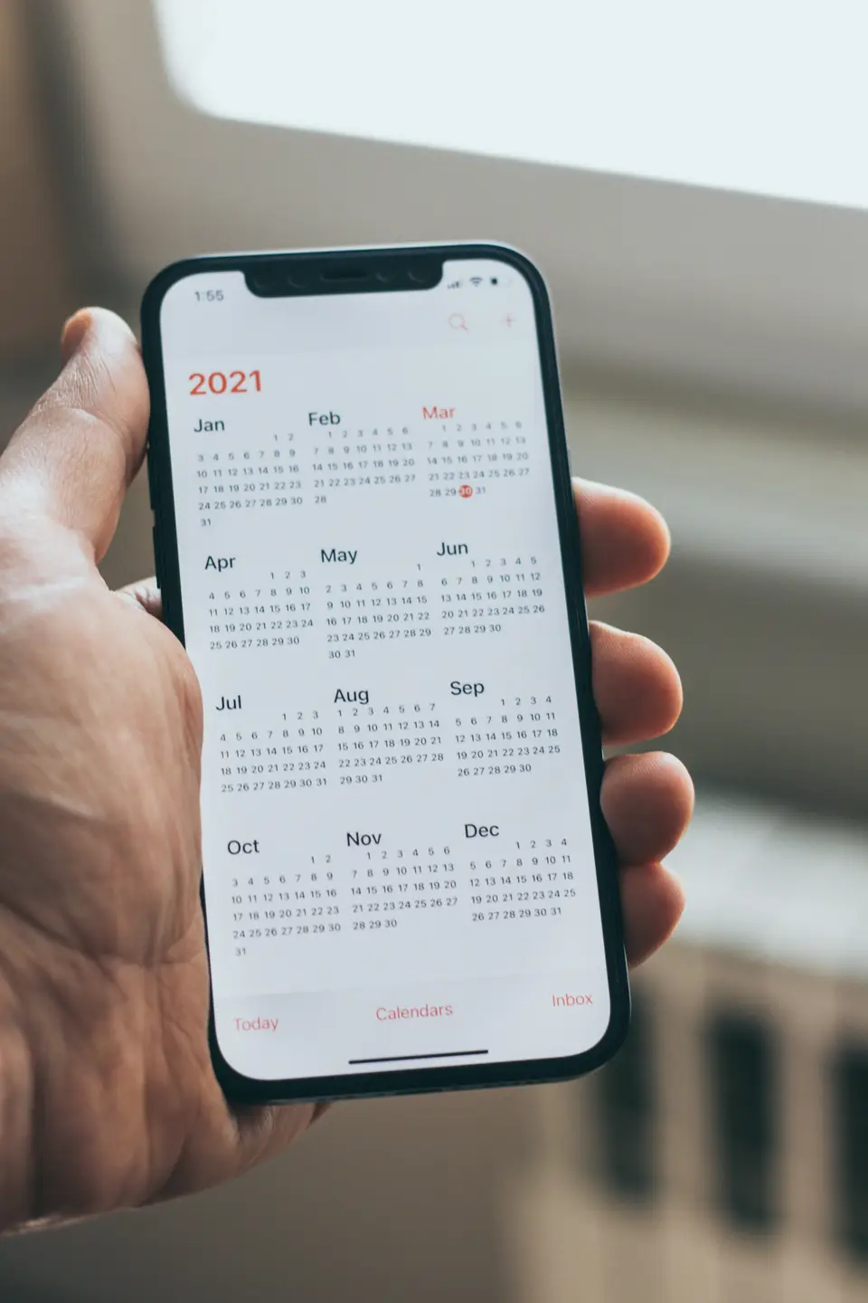 A hand holding a phone showing a full-year calendar app, thumb resting near March.