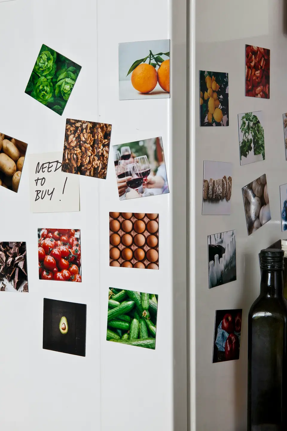 A fridge door covered in photos of fruit and vegetables cut from magazines, with a handwritten note reading 'NEED TO BUY!' pinned among them.