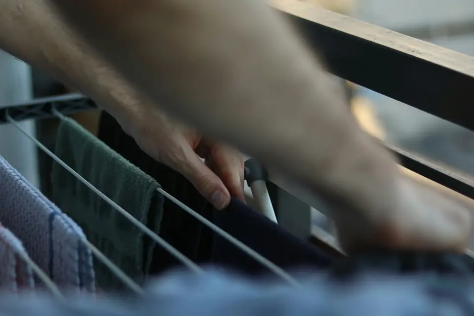 A hand reaching into a metal drying rack hung with towels and clothes, out of focus in the foreground.