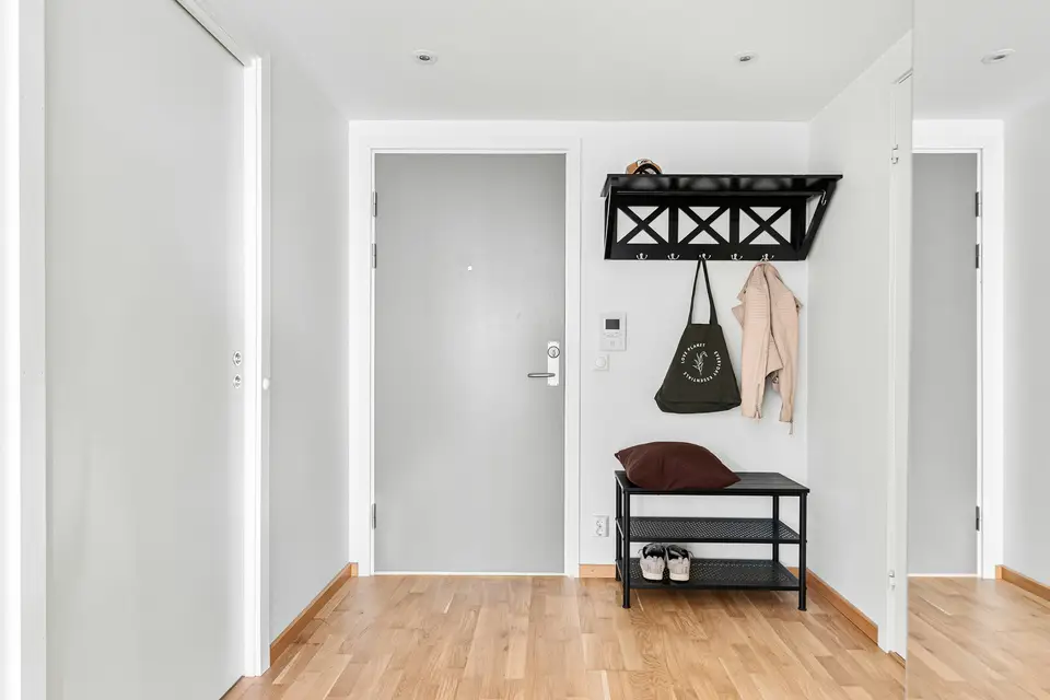 A pale hallway with a wooden bench and a coat rack beside the front door.
