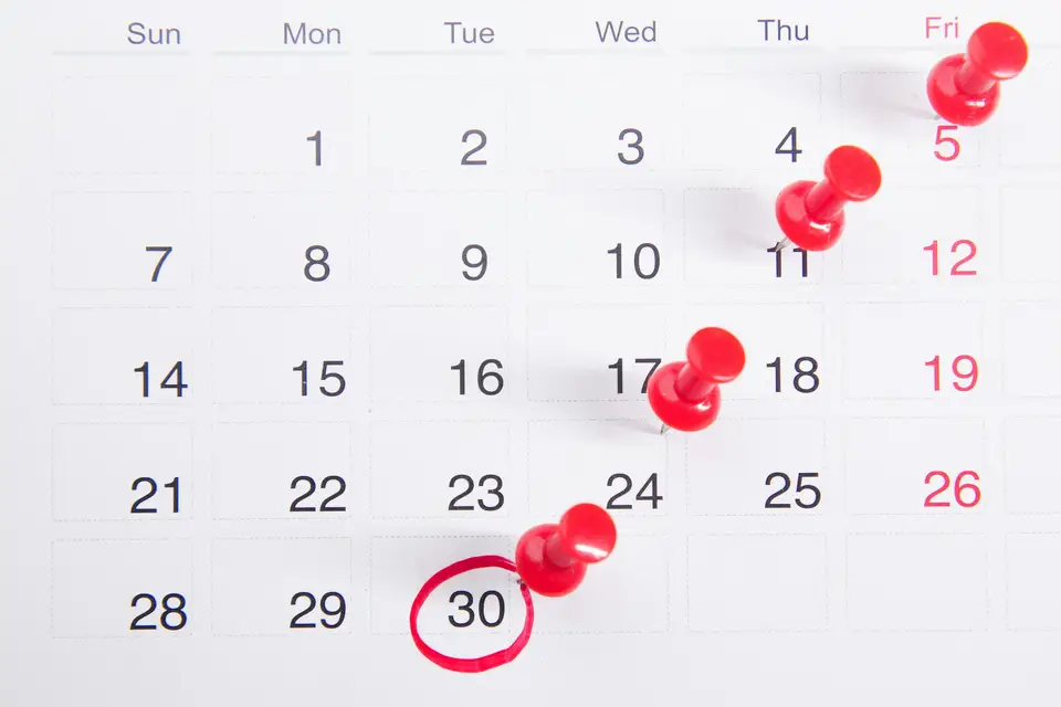A wall calendar with several dates marked by red pins and one date circled in red pen.