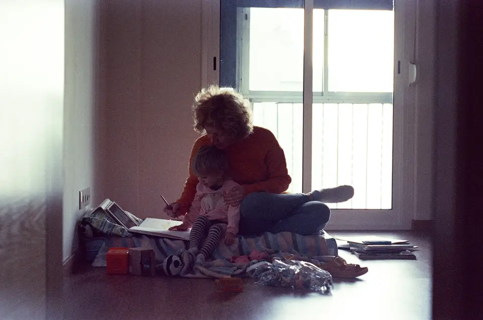 A parent and a small child sitting together on the floor in soft daylight.